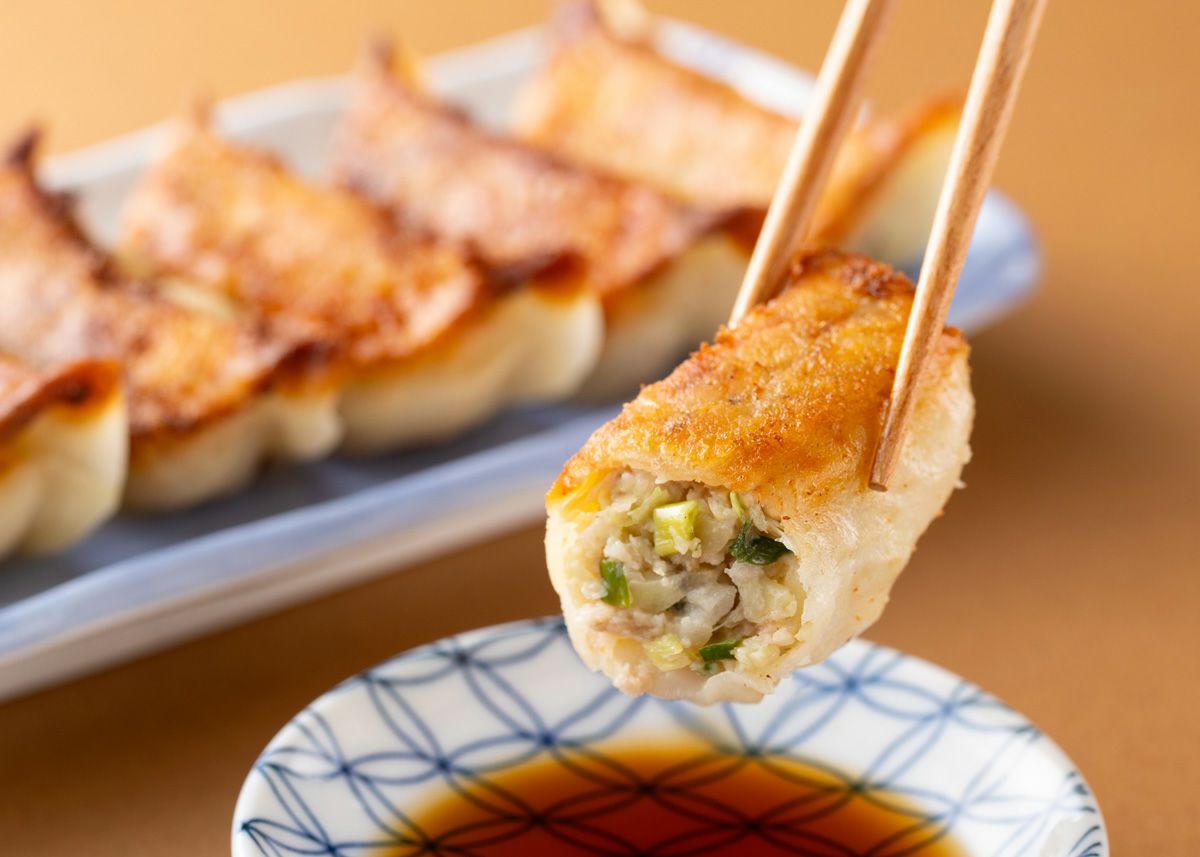 焼きあがった「将軍餃子」を箸で1粒持ち上げ、器に入ったポン酢につけている食べ方イメージ。ほどよい甘みの豚肉と特製ポン酢の相性が良い。