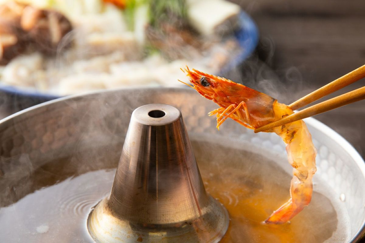 大分県産の新鮮な車海老を鍋の出汁にくぐらせ、しゃぶしゃぶしているアップ画像。プリプリとした食感が特徴の高級海老の調理イメージ。