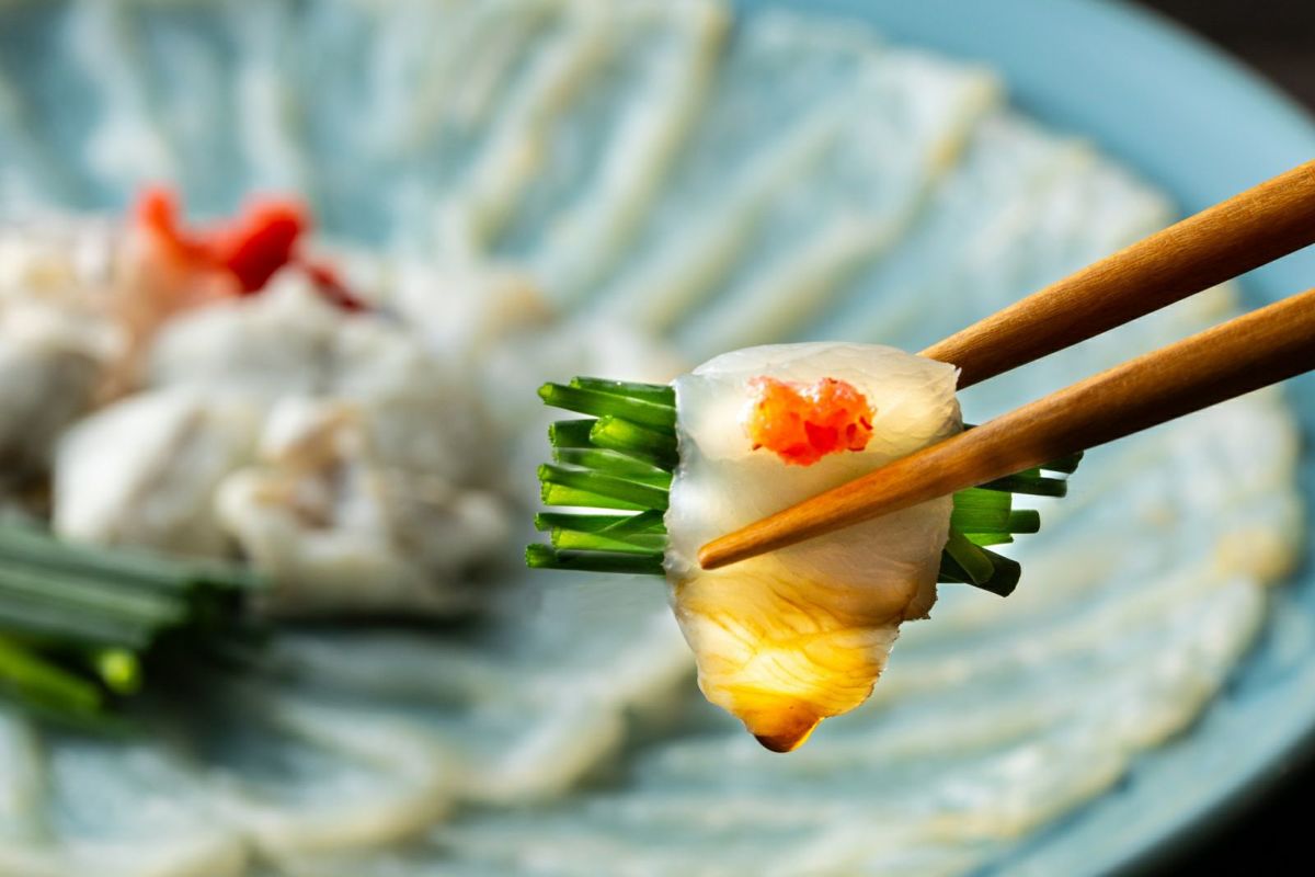 豊後とらふぐの刺身（てっさ）で刻みネギを巻いて、特製ポン酢につけているアップ画像。身の締まったふぐ刺しの食感と風味が伝わる、大分からのお取り寄せふぐ。