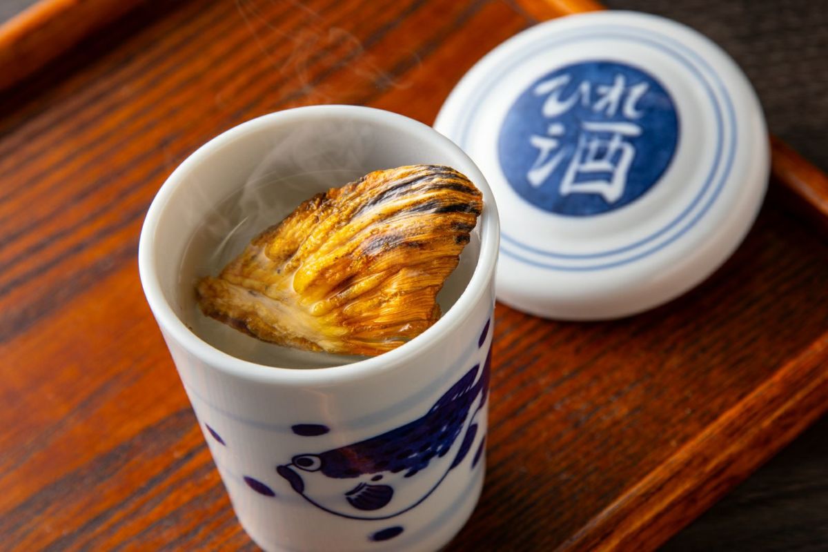 豊後とらふぐの焼きヒレが入った熱燗（日本酒）のヒレ酒画像。香ばしい風味を楽しめる大分のふぐ料理セットに付属の、贅沢なヒレ酒。