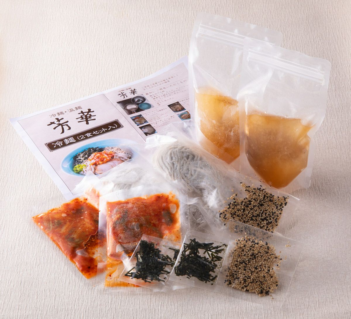 「芳華冷麺」の麺、スープ、具材、作り方が個別にパックに詰められた内容量画像。ご自宅で本格的な冷麺を簡単に楽しめるお取り寄せセット。