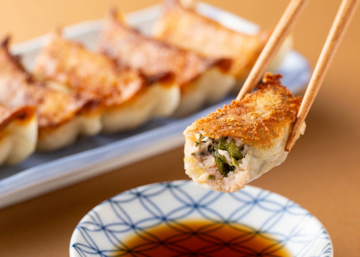 焼きあがった「しそ餃子」を箸で1粒持ち上げ、器に入ったポン酢につけている食べ方イメージ。さわやかな大葉とポン酢が絶妙にマッチする。