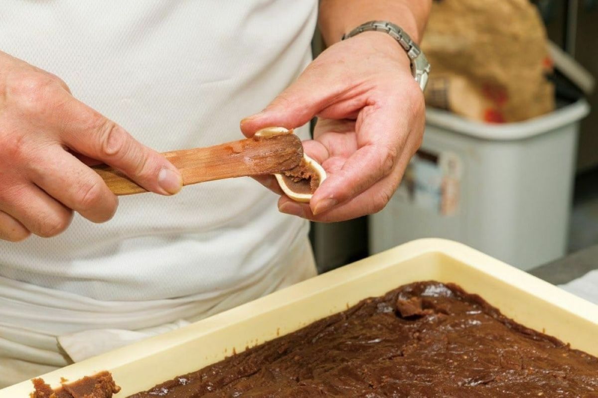 和菓子職人が「南蛮落花生チョコレートもなか」の皮に、落花生とチョコレート餡を丁寧に詰めている製造工程の画像。濃厚な餡が作られる、こだわりの手作業。
