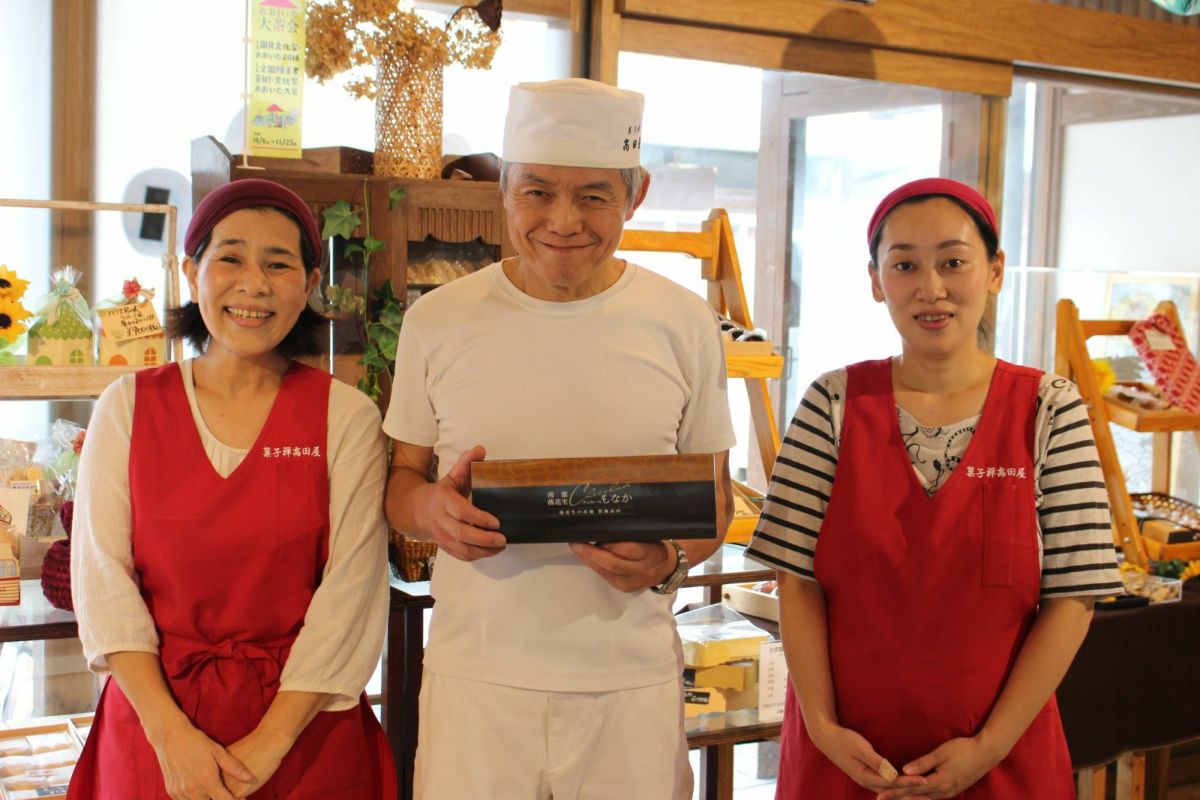 「南蛮落花生チョコレートもなか」を製造する職人と、そのご家族が並んで笑顔を見せている画像。地元に愛される、昭和の町高田屋の温かい雰囲気。