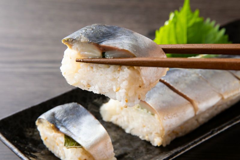 大分県産の「関さば棒寿司」（冷凍）を切って、一切れを箸で持ち上げたアップ画像。身の締まった関さばとシャリのバランスが伝わる、お取り寄せ寿司。