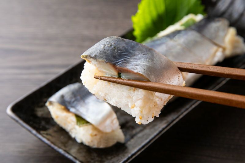 大分県産の「関さば棒寿司」（冷凍）を切って、一切れを箸で持ち上げたアップ画像。身の締まった関さばとシャリのバランスが伝わる、お取り寄せ寿司。