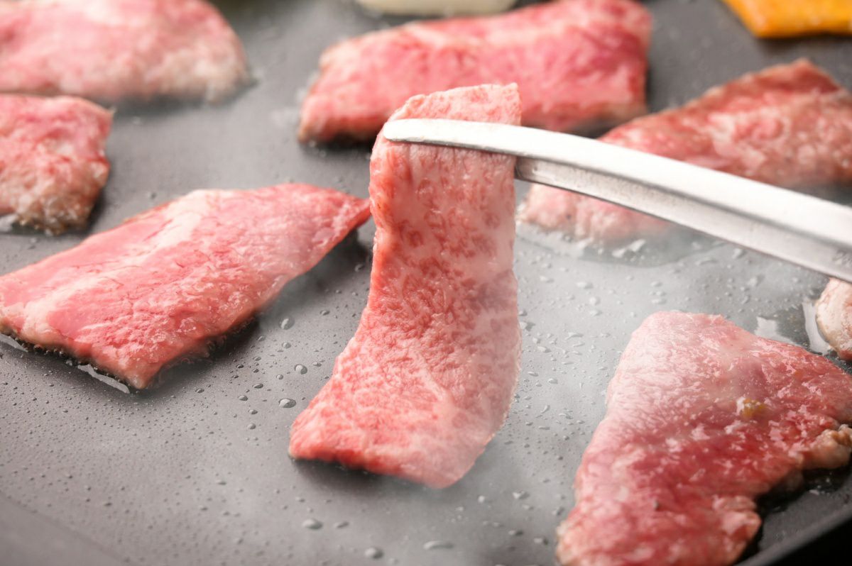 大分県産「おおいた和牛」の肉を鉄板または網で焼いている調理中の画像。上質な脂がジュージューと音を立てて溶け出し、食欲をそそる高級焼肉風景。
