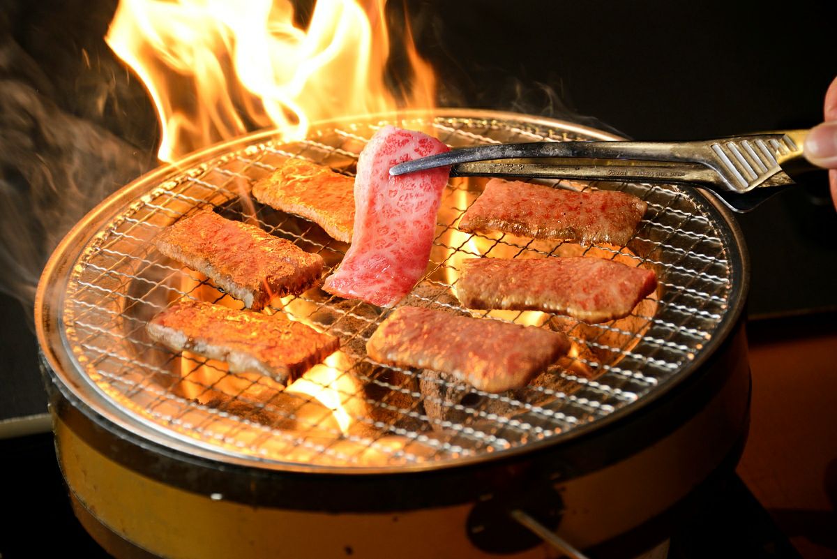 大分県のブランド牛「おおいた和牛」をいろり（囲炉裏）で焼いている調理中の画像。霜降りの美しい和牛の焼肉は、豪華なバーベキュー（BBQ）やお祝いの席に最適な一品。